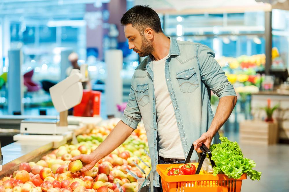 Making nutritional choice.Confident young man holding apple and shopping bag while standing in a food store